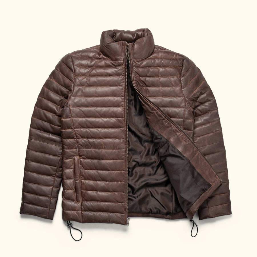 Man wearing a brown quilted jacket, standing outdoors with a thoughtful expression.