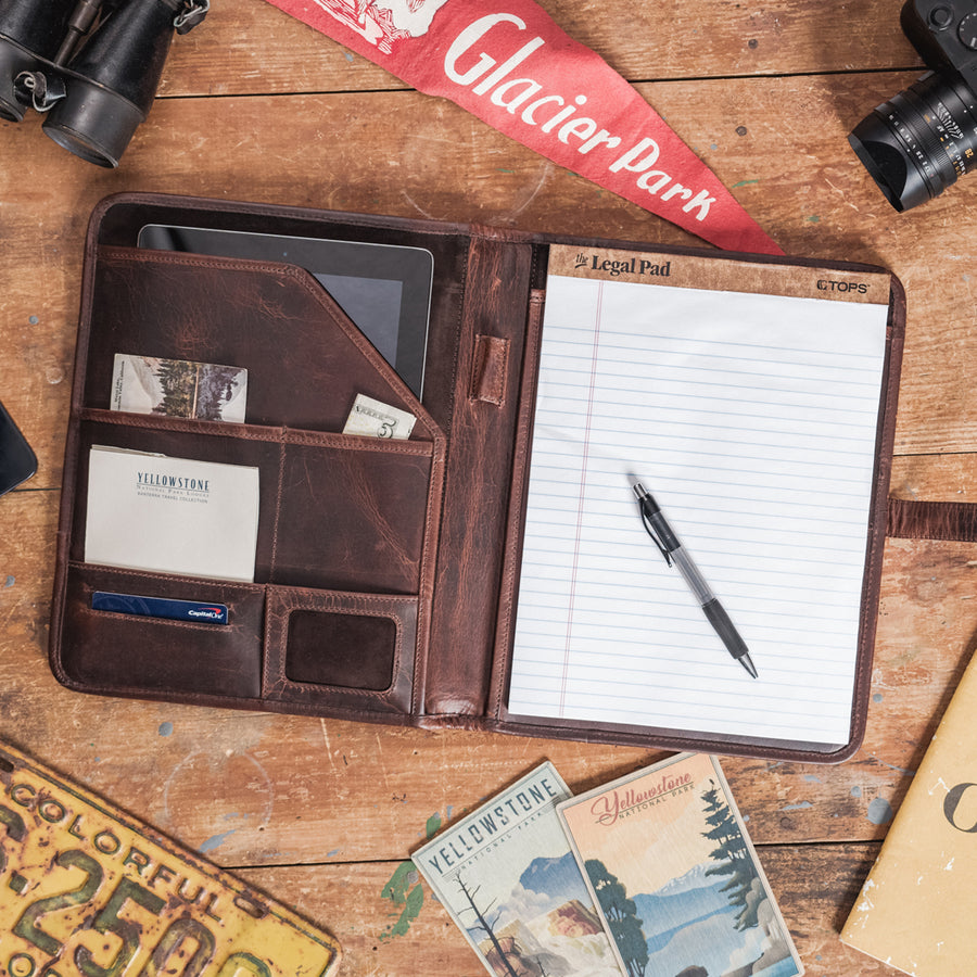 Dark oak Roosevelt leather travel padfolio with secure cross closure and vintage design on a rustic table.