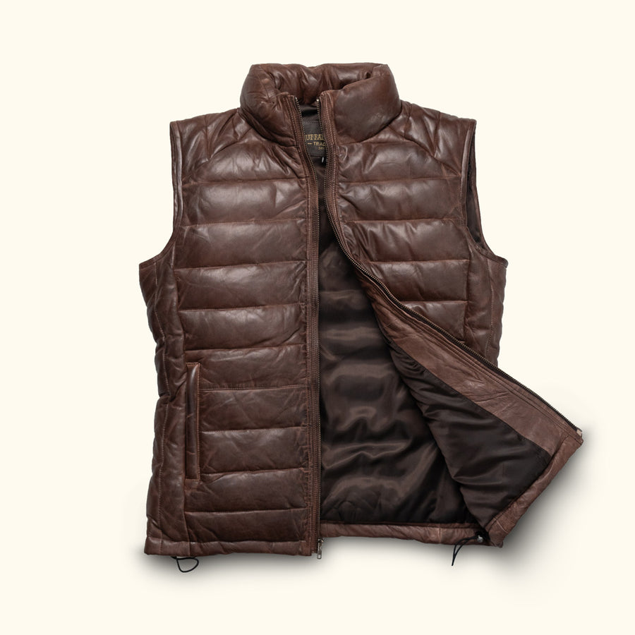 Outdoorsman in a brown puffer vest, walking and gazing into the distance with binoculars in hand.