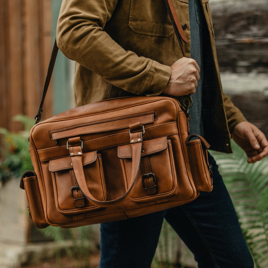 Amber brown Roosevelt buffalo leather pilot bag featuring multiple pockets, adjustable straps, and durable metal hardware.