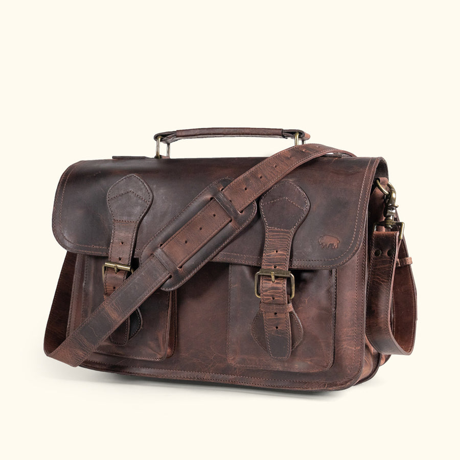 Man holding a dark oak Roosevelt leather briefcase with antique brass buckles and adjustable shoulder strap.